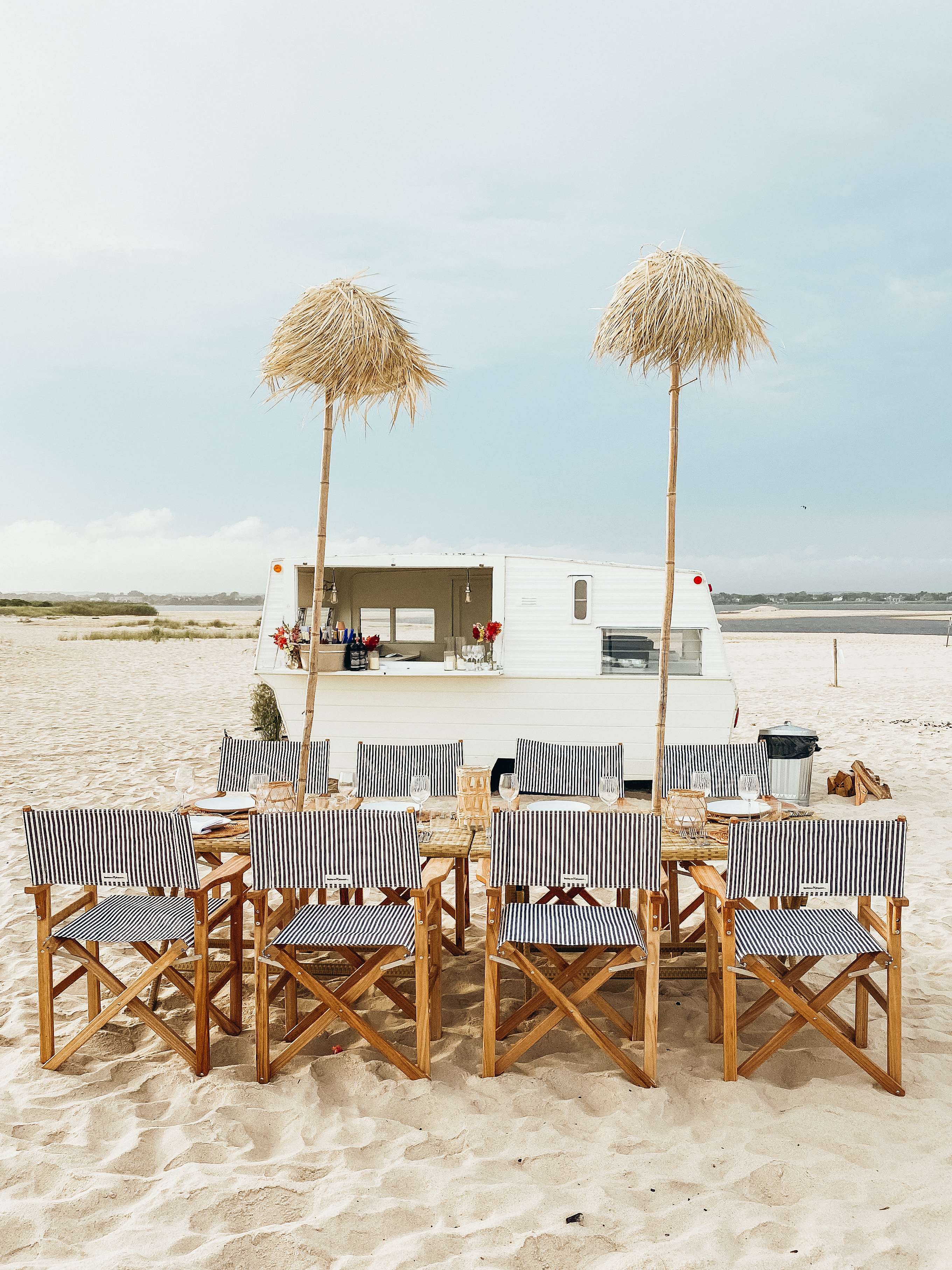 Beachfront dinner setting with striped chairs and mobile bar